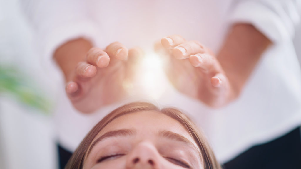 Close-up image of a relaxed young woman receiving Reiki therapy